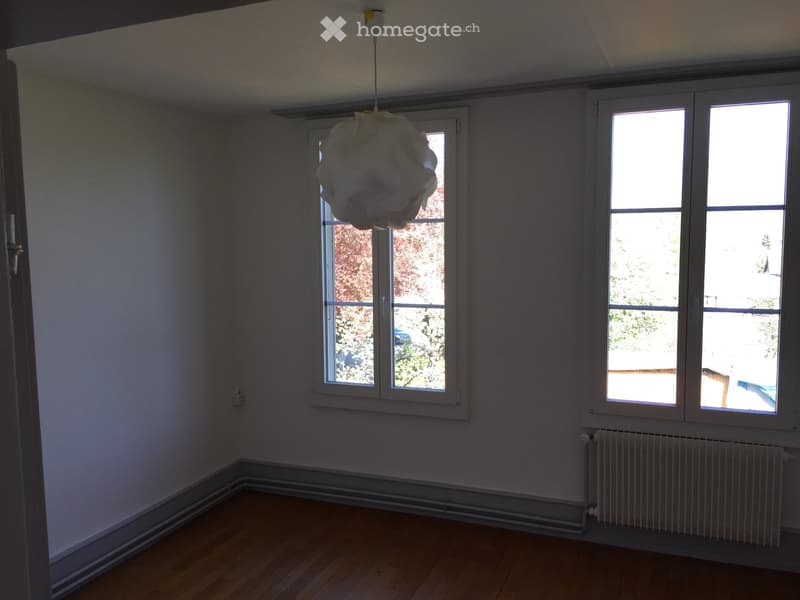 Empty room with wooden flooring, white walls, large windows, and a radiator. No furniture or equipment present.