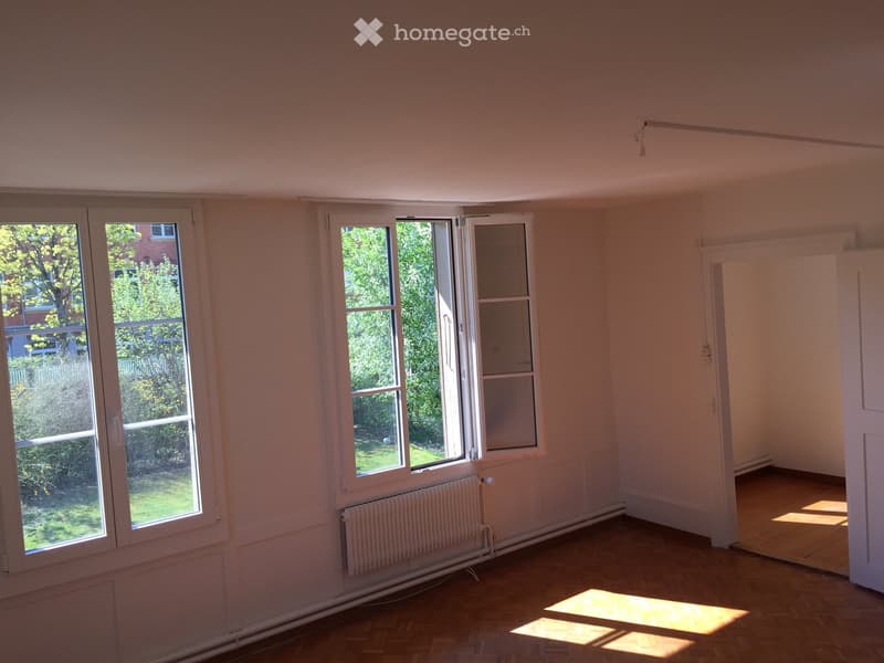 Empty room with wooden flooring, large windows, and radiators. No furniture or equipment present.