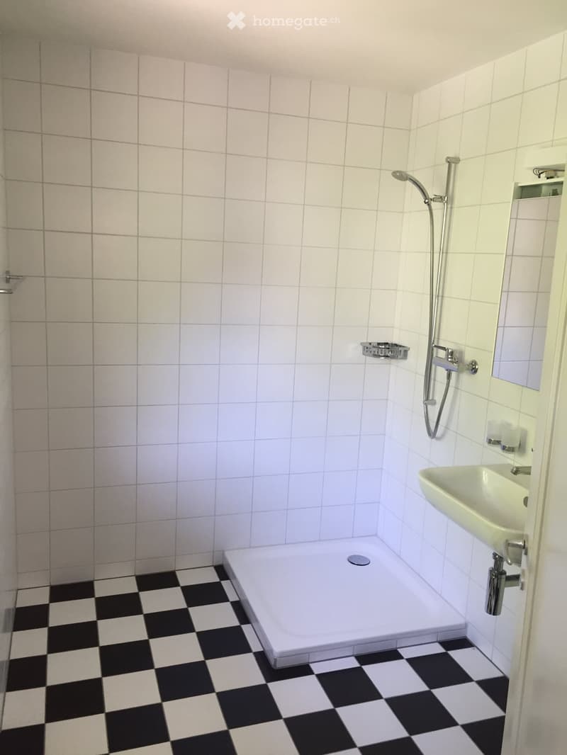 Modern bathroom with white tiled walls, black and white checkered floor, bathtub, sink, and showerhead.