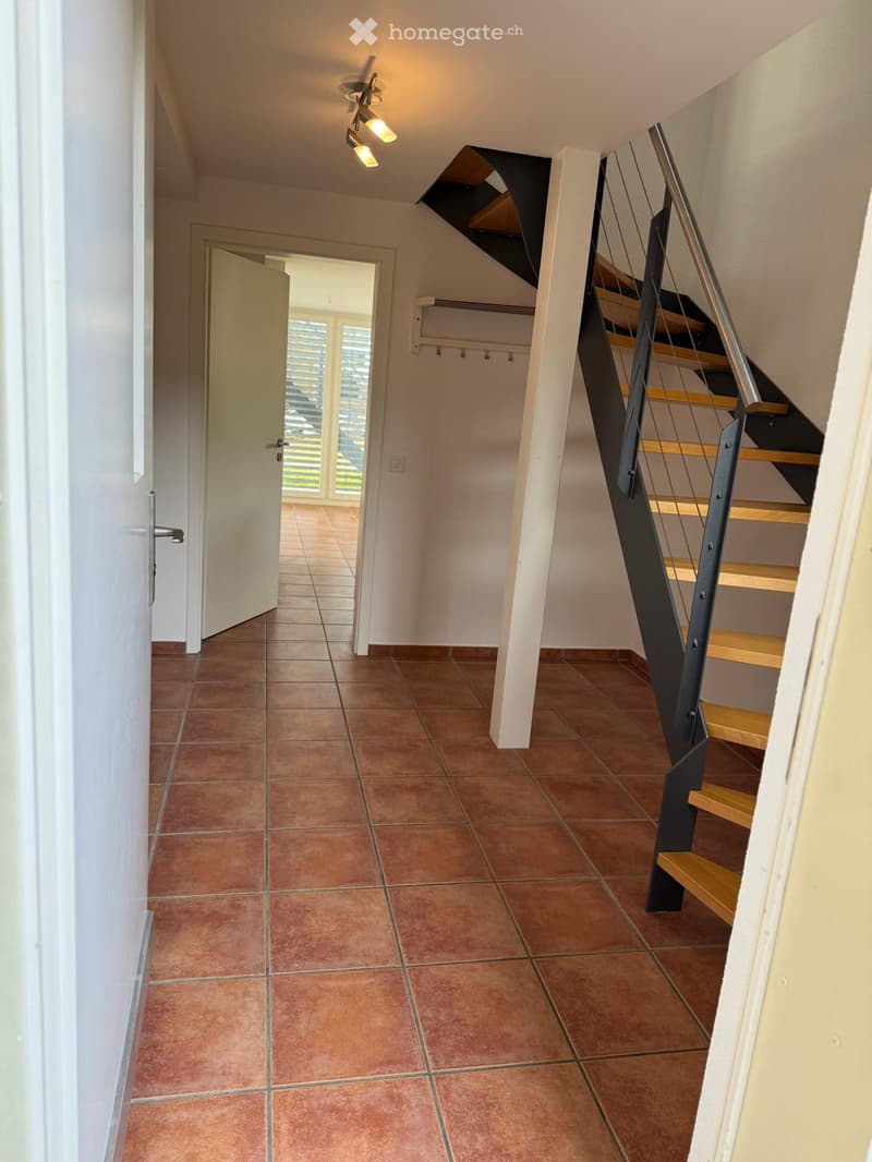 Hallway with terracotta tiled floor, modern staircase with wooden steps and metal railing, white walls, and recessed lighting.