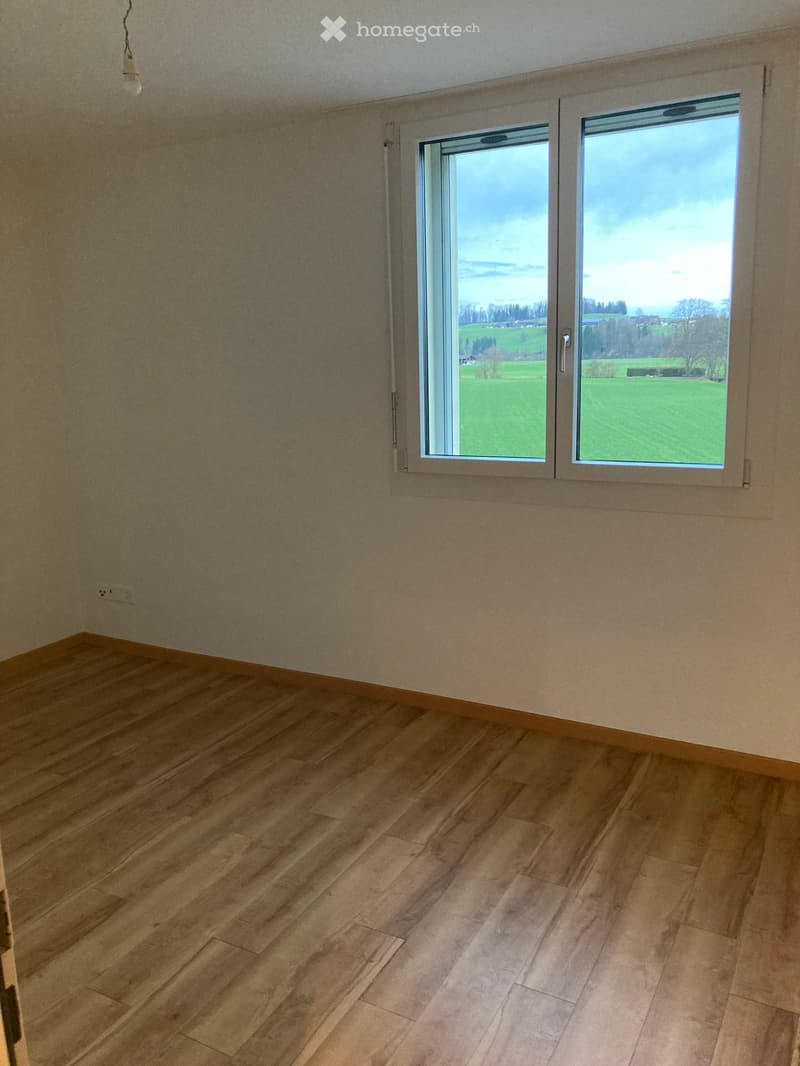 Empty room with wooden flooring and large windows offering a view of a green field.