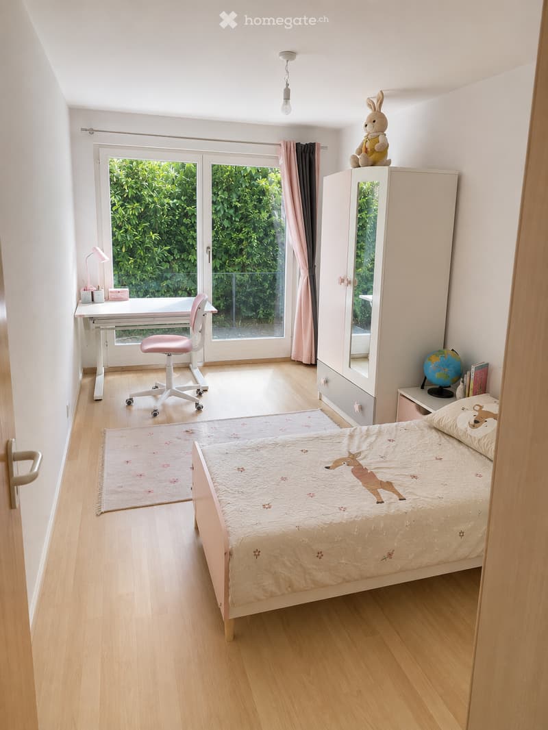 Bright, modern bedroom with a single bed, desk, chair, wardrobe, and a view of greenery through large windows.