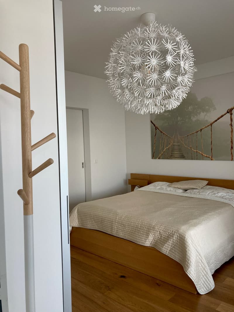 White walls, wooden floor, double bed, chandelier, photo on wall