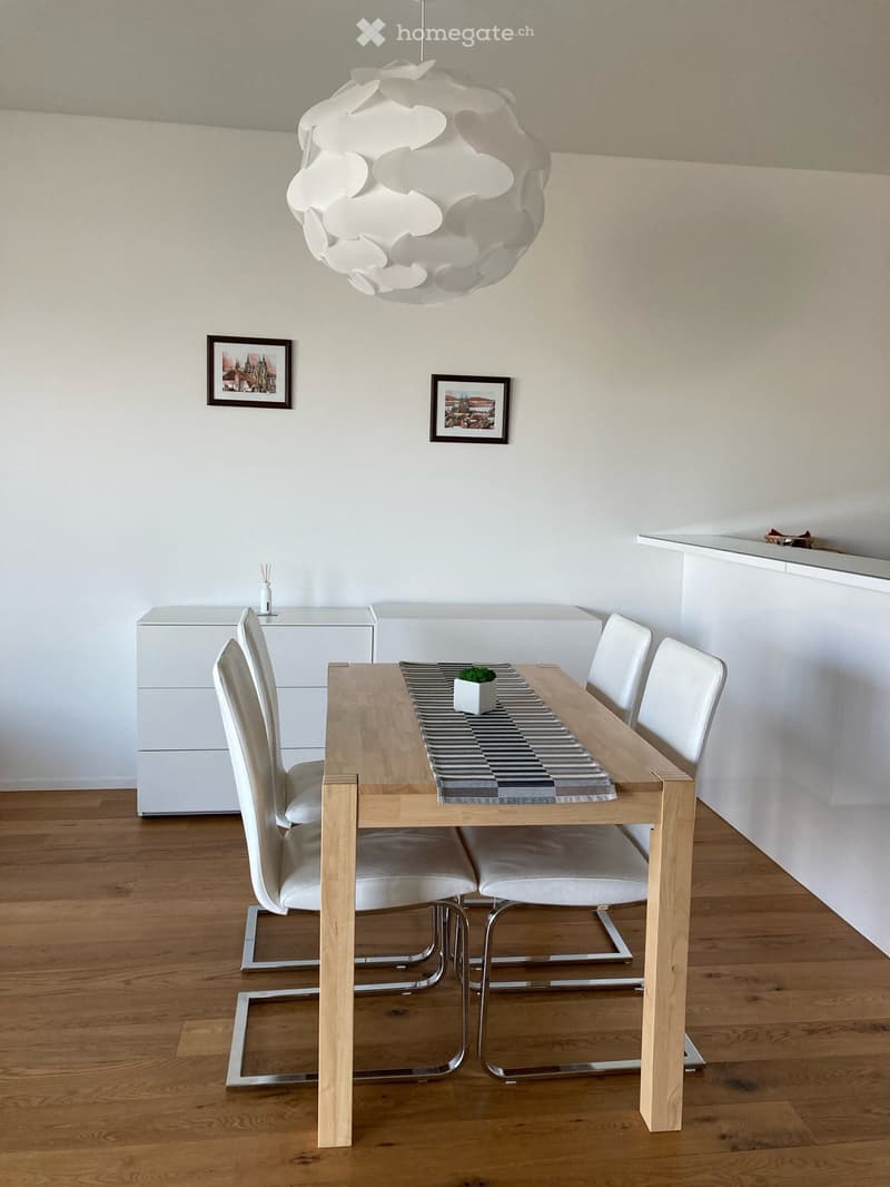 dining room, wooden floor, modern dining table, four white chairs, wooden table lamp, two frames on the wall, white cabinets, striped table mat