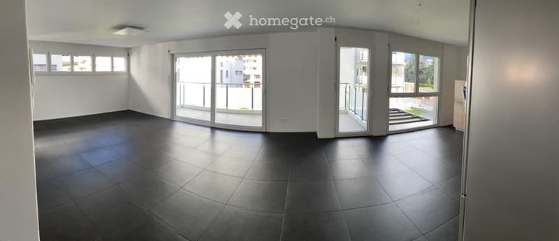 Empty room with dark tiled floor, white walls, large sliding glass doors leading to a balcony, and several windows allowing natural light.