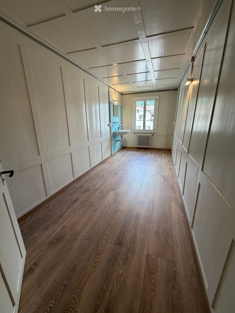 Empty hallway with wooden flooring, white walls, and a small bathroom visible at the end.