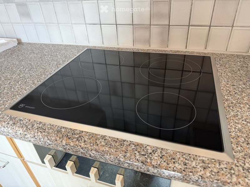 Modern kitchen with granite countertop and sleek black induction cooktop featuring four circular cooking zones.