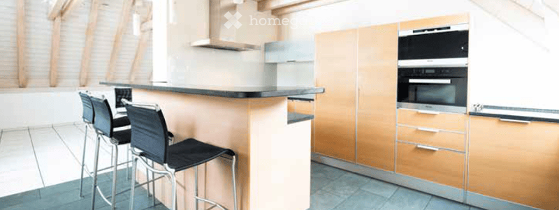 Modern kitchen with light wood cabinets, black countertop, built-in oven, and bar stools.