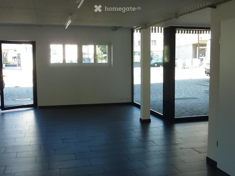 Empty room with dark tiled floor, white walls, large windows, and glass doors leading to an outdoor area.