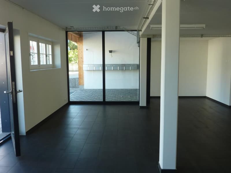 Empty hallway with dark tiled floor, white walls, and large glass doors leading to an outdoor area.