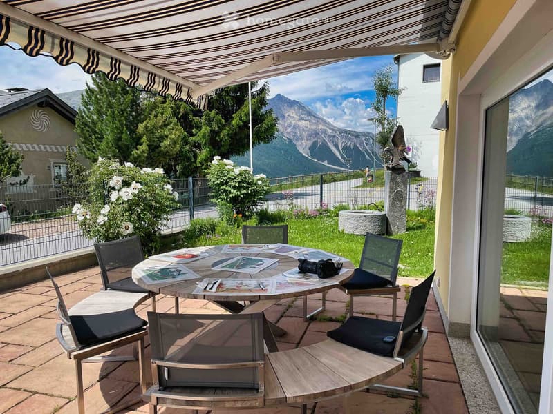 Balcony with a round table, chairs, and a view of mountains and greenery.