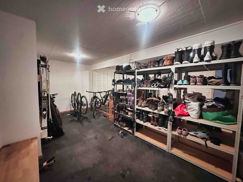 Storage area with metal shelves filled with boots and shoes, bicycles, and a ski leaning against the wall.