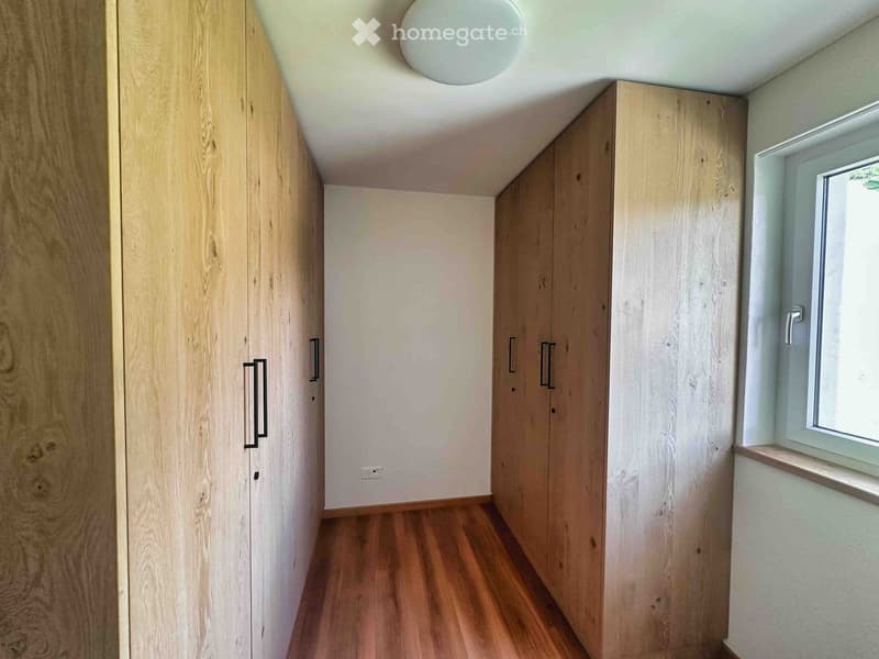 Empty hallway with wooden flooring, light wooden built-in wardrobes, and a window on the right side.