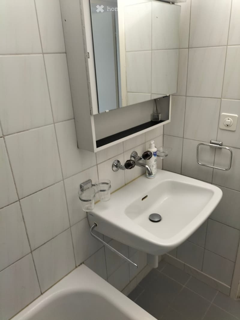 Bathroom with white tiled walls, a white sink with a chrome faucet, a mirror cabinet, and a towel ring.