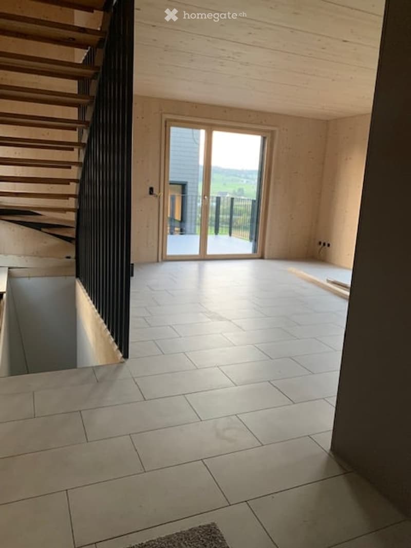Empty room with wooden walls, tiled floor, staircase leading up, and large sliding glass door opening to a view.