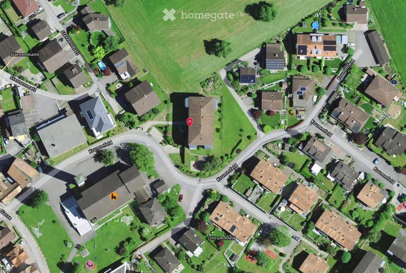 Aerial view of a residential area with multiple houses, green lawns, and surrounding streets.