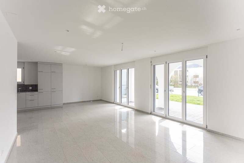 Bright, empty room with white walls, tiled floor, and large sliding glass doors leading to an outdoor area. Minimalist design with built-in cabinets visible on one side.