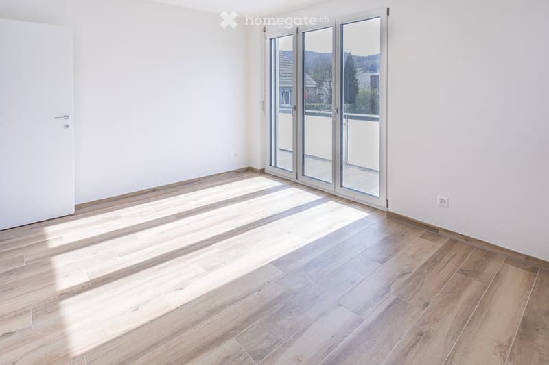 Empty room with wooden flooring, white walls, and large glass sliding doors leading to a balcony.