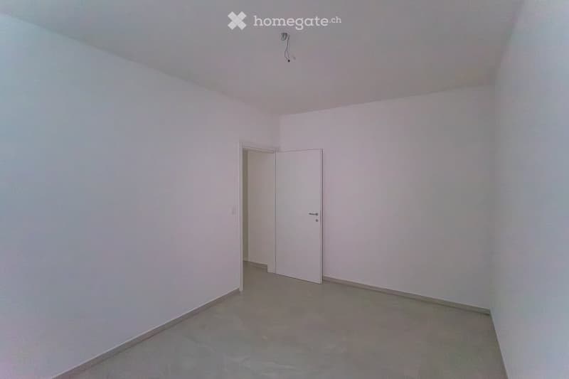 Empty room with white walls, grey concrete floor, and a single white door.