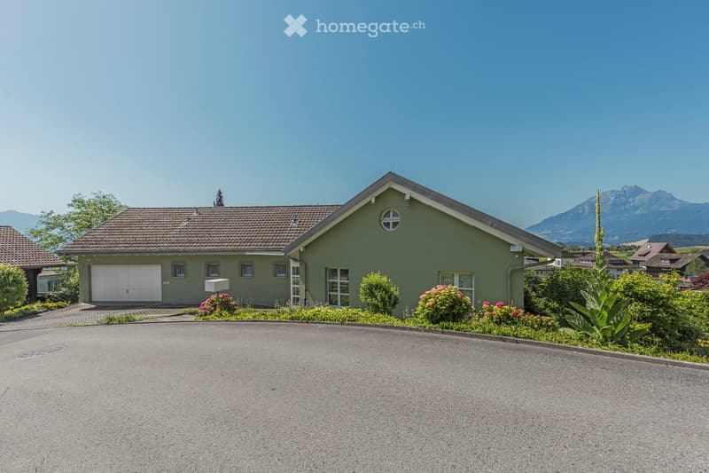 Two-story house with a garage, surrounded by a well-maintained garden and scenic mountain backdrop.