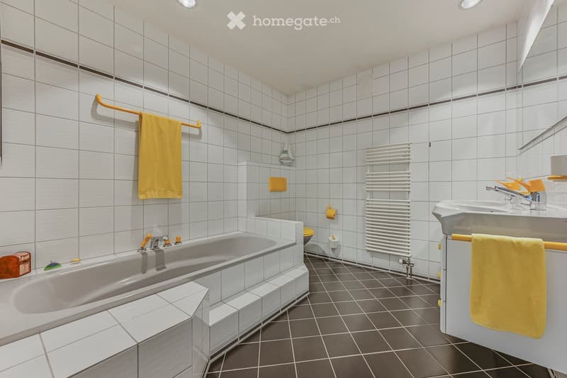 Modern bathroom with white tiled walls and dark tiled floor, featuring a bathtub, sink, radiator, and towels.