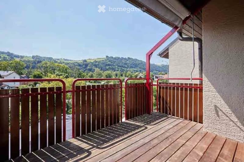Balcony with wooden decking, red metal railings, and scenic mountain view in the background.