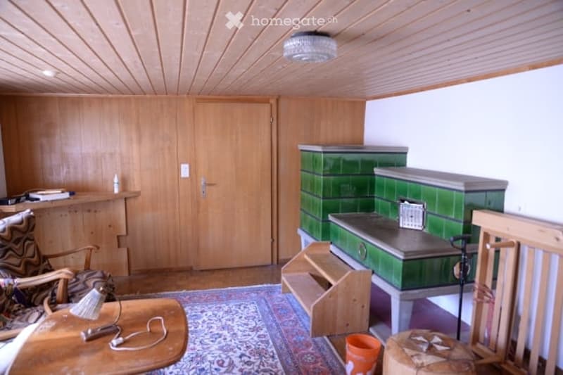 A cozy, wooden-paneled room with a sofa, small table, chair, and a cabinet. The room features a patterned rug and a wooden door leading to another space.