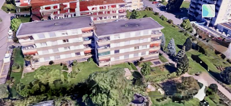 Aerial view of a multi-story residential building with numbered units, surrounded by greenery and other structures.