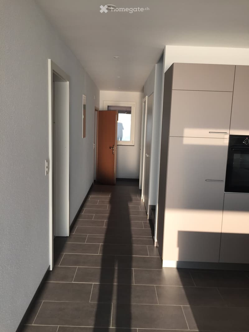 a narrow hallway with tiled flooring, three doors, one open with a window and shadow cast on the floor