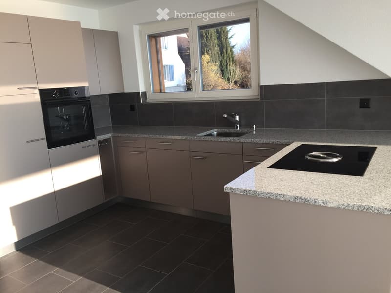 Modern kitchen with a grey tiled floor, a white counter top, a granite sink, a gas stove, and built-in cabinets with white doors. An oven is positioned below a window overlooking the outdoors.