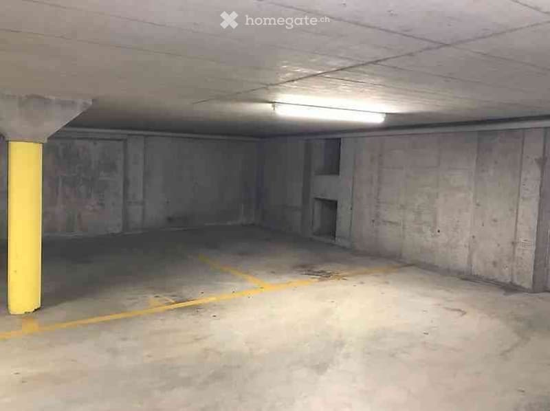Empty underground parking space with concrete walls, a single yellow support column, and a marked parking area.