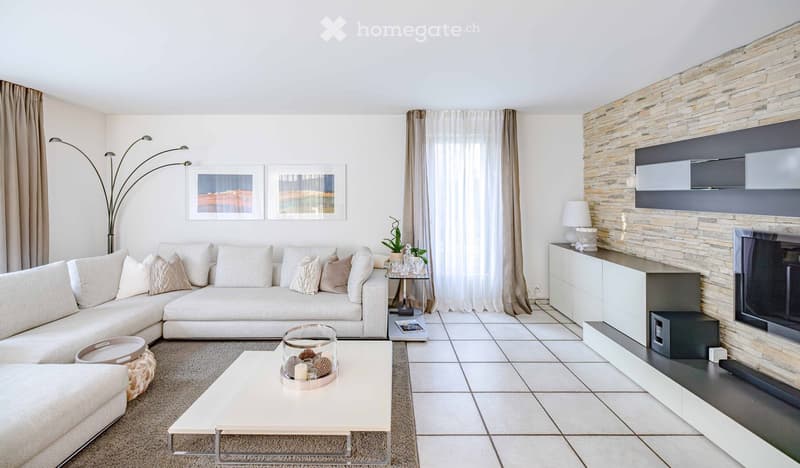 Modern living room with a white sectional sofa, coffee table, side table, floor lamp, TV mounted on a stone accent wall, and decorative items.
