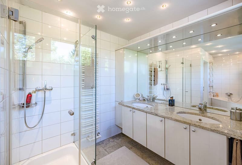 Modern bathroom with a large walk-in shower, double sink vanity, and a bathtub. Features include white tiles, a large mirror, and built-in storage cabinets.