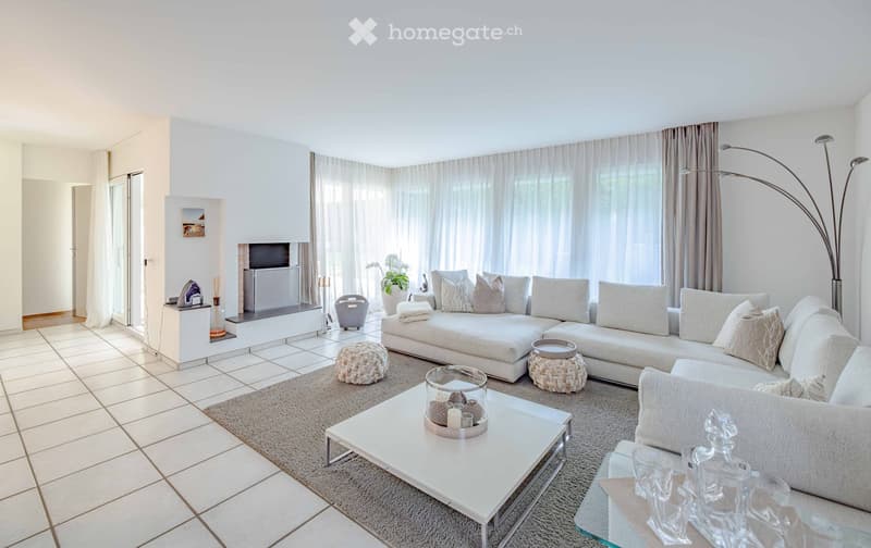 Modern living room with large windows, white sofa, coffee table, floor lamp, and decorative items.