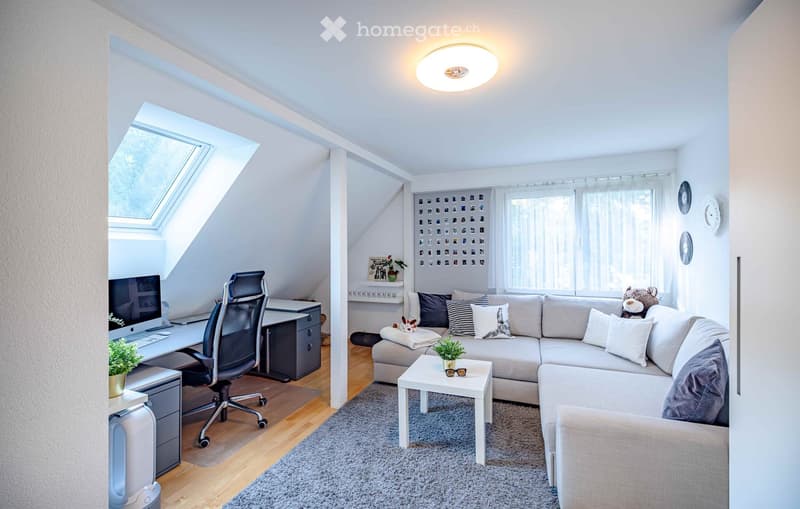 A modern, multi-functional room with a living area and a workspace. Features a large sectional sofa, coffee table, desk with computer, and decorative plants.