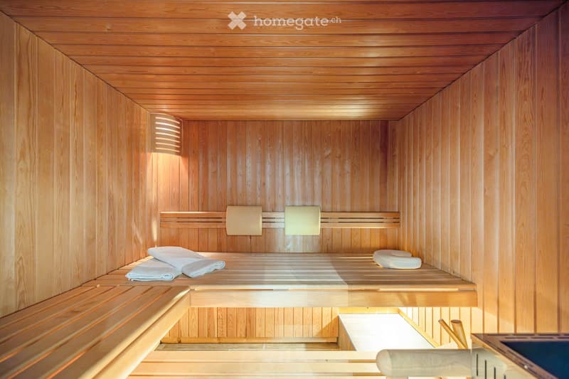Wooden sauna with benches, towels, and a small control panel.