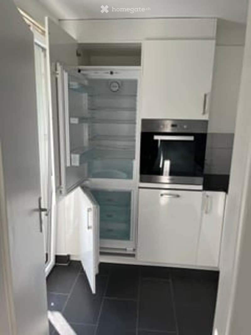Modern kitchen with white cabinets, black tiled floor, open refrigerator, and built-in oven.