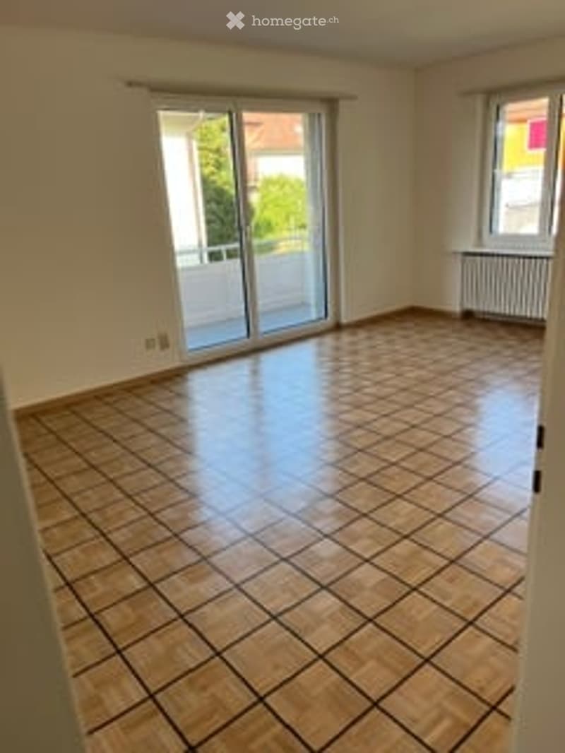 Empty room with tiled floor, large sliding glass door leading to a balcony, and a window with radiator.