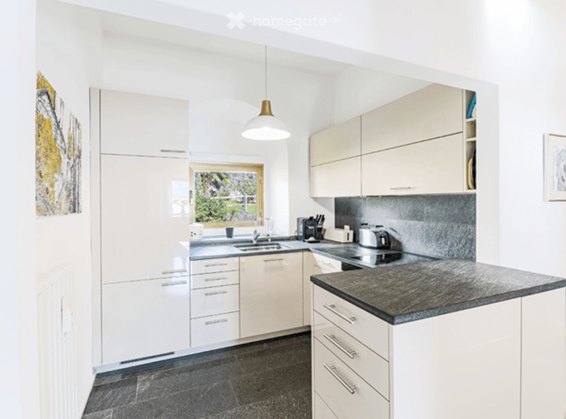 Modern kitchen with white cabinets, granite countertop, stainless steel appliances, and a view through a window.