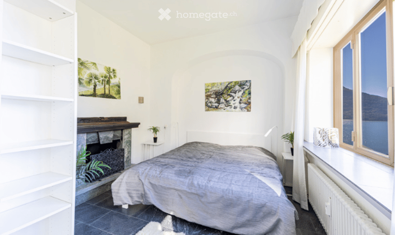 Cozy bedroom with a large bed, fireplace, shelves, and a view of the lake through large windows.