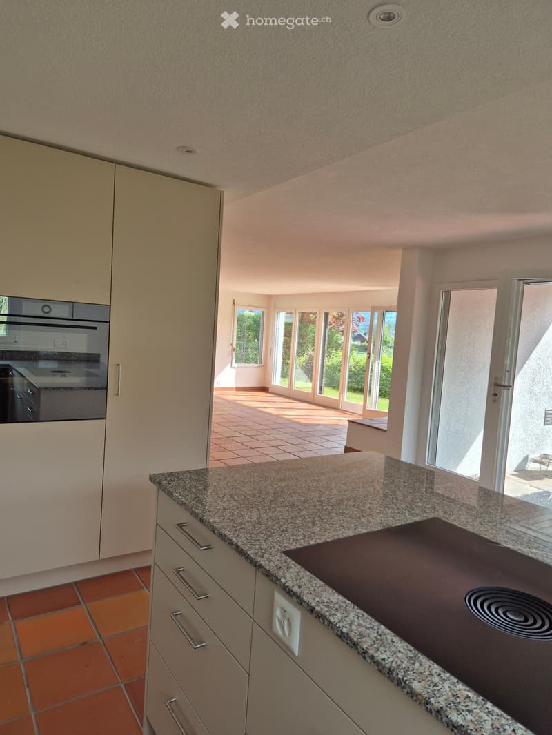 Modern kitchen with granite countertop, induction cooktop, built-in oven, and light-colored cabinets.