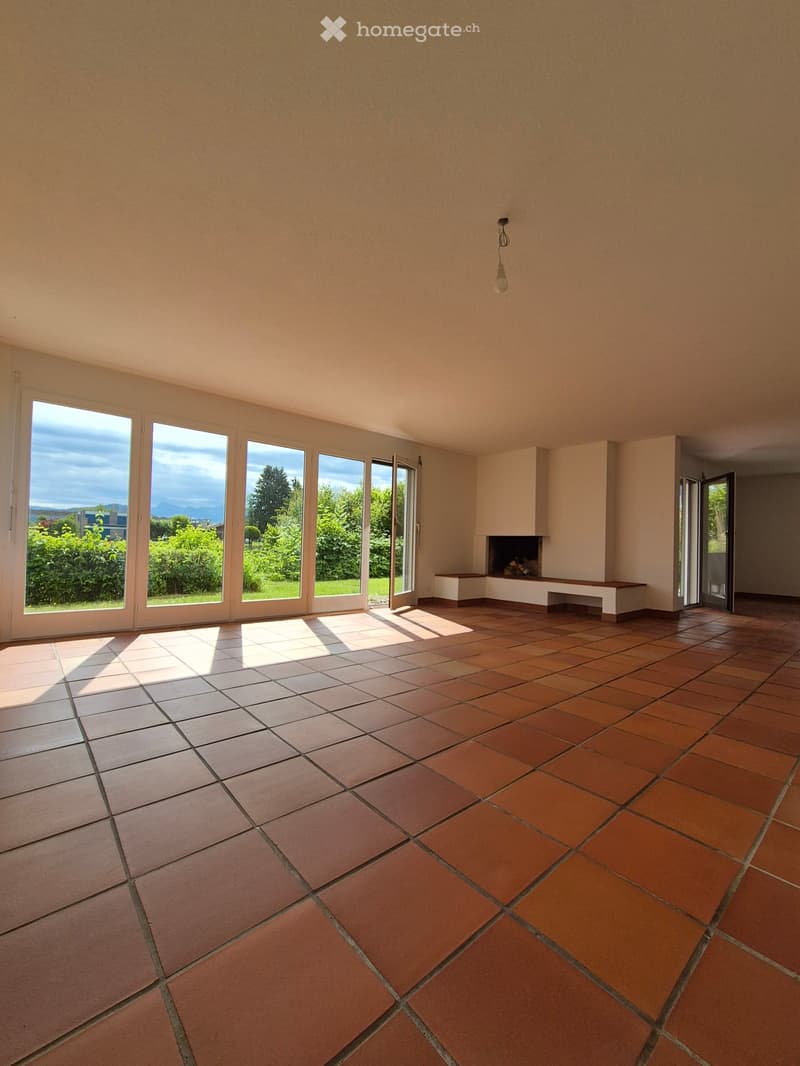 Empty room with tiled floor, large windows, fireplace, and bench.