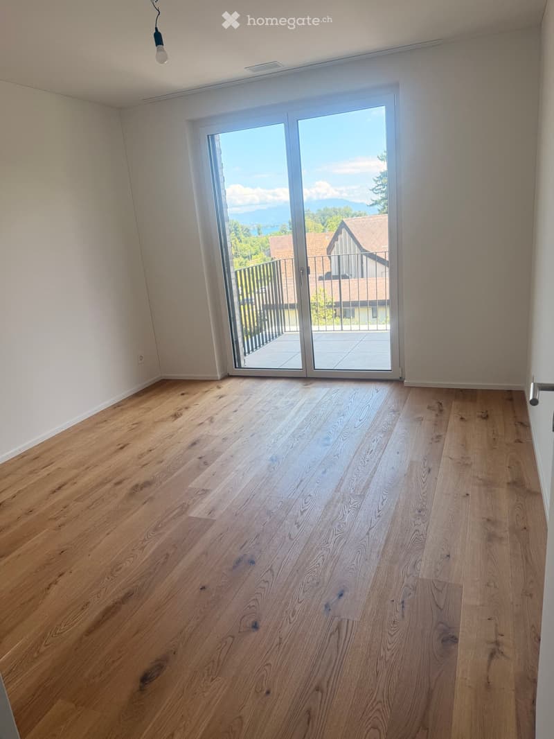 Empty room with light wooden flooring and large sliding glass doors leading to a balcony with a scenic view.
