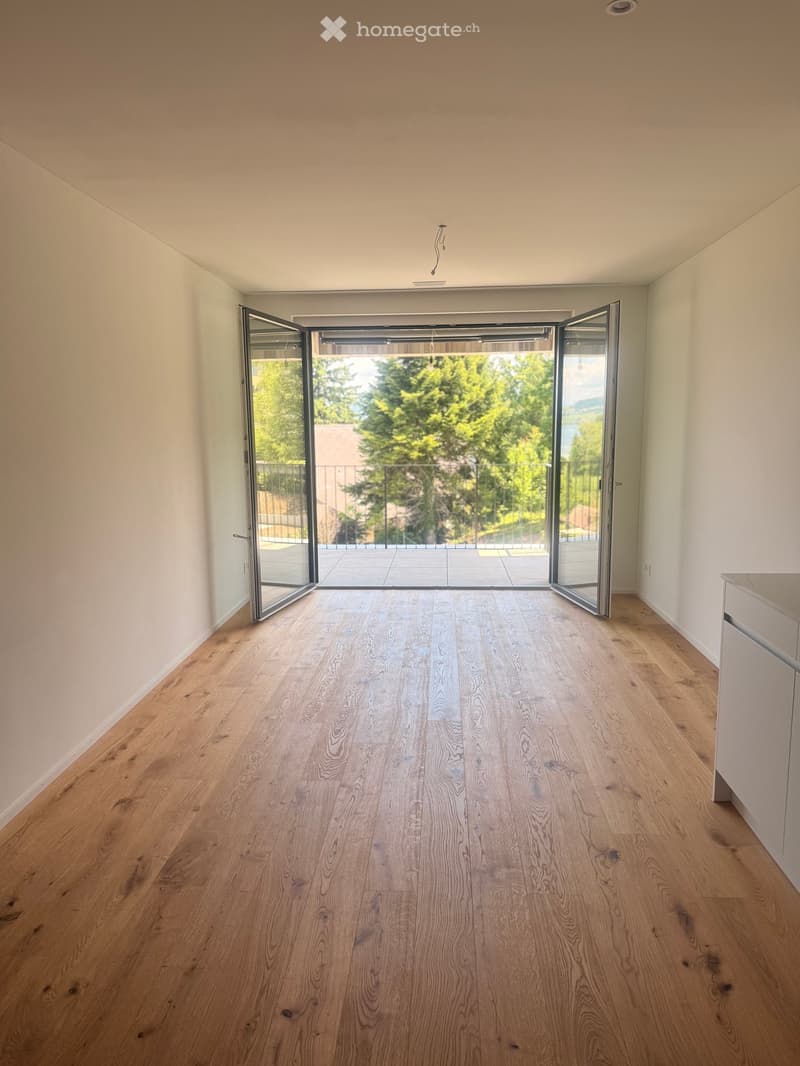 Empty room with light wooden flooring, white walls, and large glass sliding doors leading to a balcony with outdoor view.
