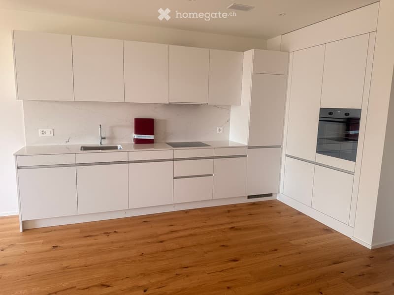 Modern kitchen with white cabinets, marble countertops, and wooden flooring. Features a sink, faucet, and built-in oven.