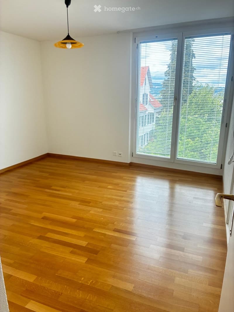 Empty room with wooden flooring, white walls, large sliding glass door, and a hanging light fixture.
