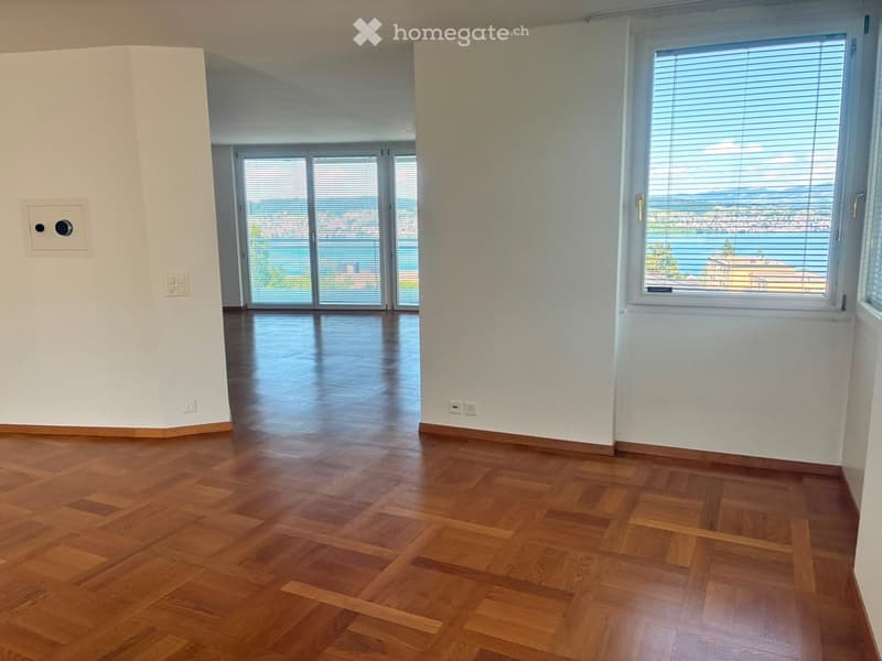 Empty room with wooden flooring, large windows, and sliding glass doors leading to a balcony with scenic views.