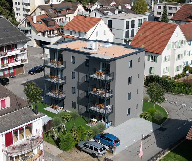 4-story apartment building, balconies on multiple floors, green lawn, multiple parked cars