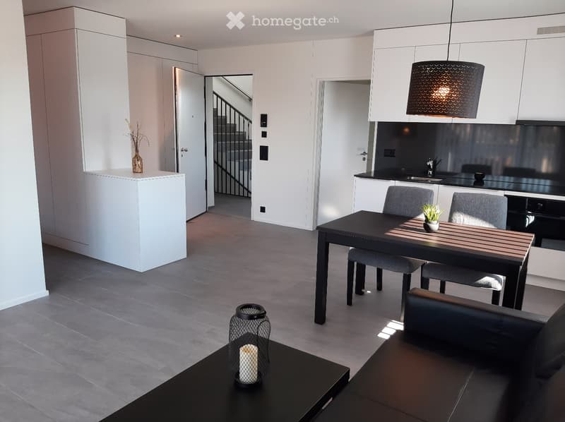 open plan living room with dining area, gray flooring, black dining table with chairs, black sofa, white cabinets, modern pendant lamp, staircase, coffee table with candle