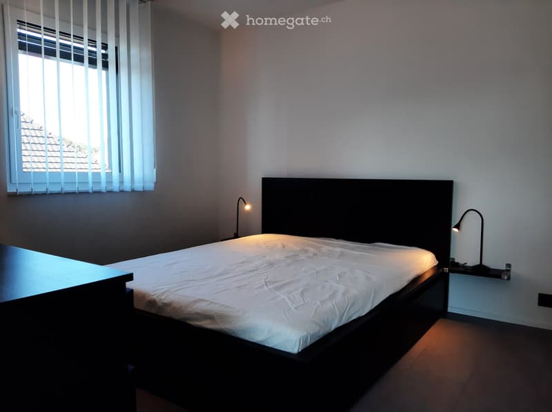 Bedroom with a bed, desk, two lamps on the nightstands, and a window with blinds